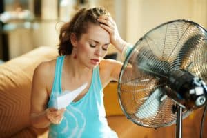 unhappy housewife in the modern house in sunny hot summer day in the front of working fan suffering from summer heat