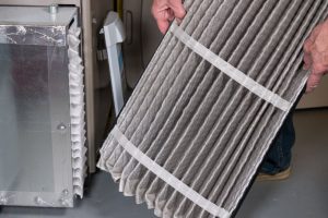 Senior man examining a folded dirty air filter in the HVAC furnace system in basement of home