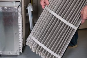 Senior man examining a folded dirty air filter in the HVAC furnace system in basement of home