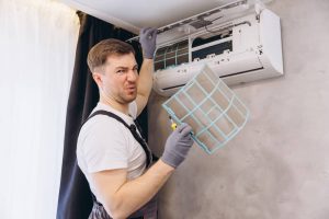 Repairman holding a grimy air conditioner filter, looking disgusted while inspecting it during routine maintenance work indoors