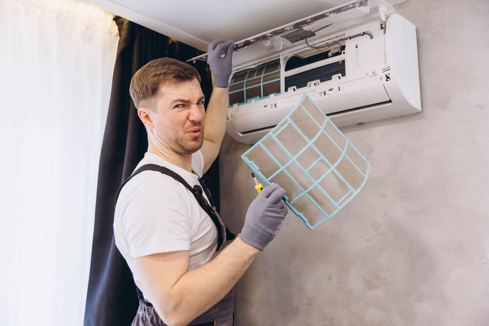 Repairman holding a grimy air conditioner filter, looking disgusted while inspecting it during routine maintenance work indoors
