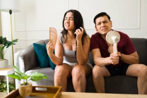 Sweating couple relaxing indoors, escaping scorching summer temperatures by lounging together on comfortable living room sofa