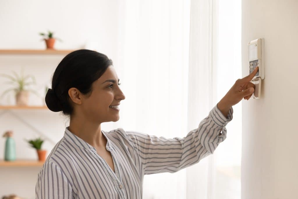 Happy millennial female homeowner managing smart house electronic system pressing button at control panel. Young mixed race woman confident in easy programming of modern climate control device