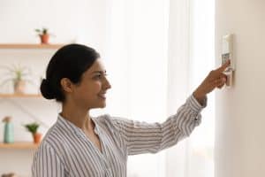 Happy millennial female homeowner managing smart house electronic system pressing button at control panel. Young mixed race woman confident in easy programming of modern climate control device