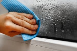 high humidity in the house. hand wipes off water condensation from plastic window glass in the room. home moisture