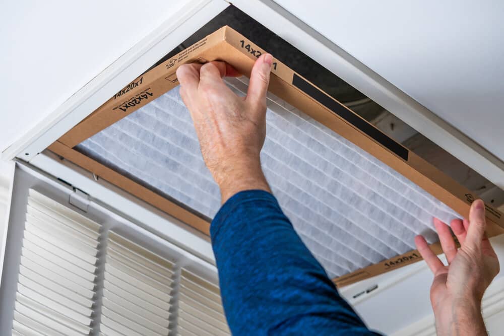 Man replacing dirty HVAC air filter in ceiling vent. Home air duct system maintenance for clean air.