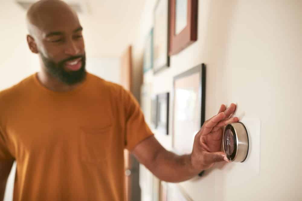 Man Adjusting Digital Central Heating Thermostat At Home
