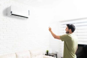 Smiling man turning on ductless mini split air conditioner with remote control in living room at home