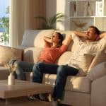 Happy couple relaxing sitting on a couch with arms on head at sunset at home