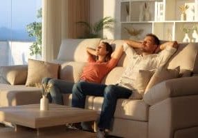 Happy couple relaxing sitting on a couch with arms on head at sunset at home