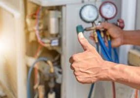 Close up of thumbs up in front of repairman fixing HVAC system