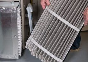 Senior man examining a folded dirty air filter in the HVAC furnace system in basement of home