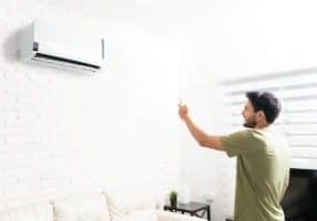 Smiling man turning on ductless mini split air conditioner with remote control in living room at home