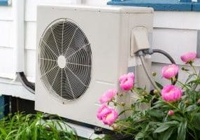 Air conditioning/ Heat pump unit on the side of a home among the flowers.