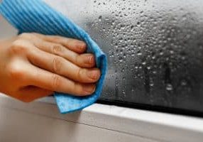 high humidity in the house. hand wipes off water condensation from plastic window glass in the room. home moisture
